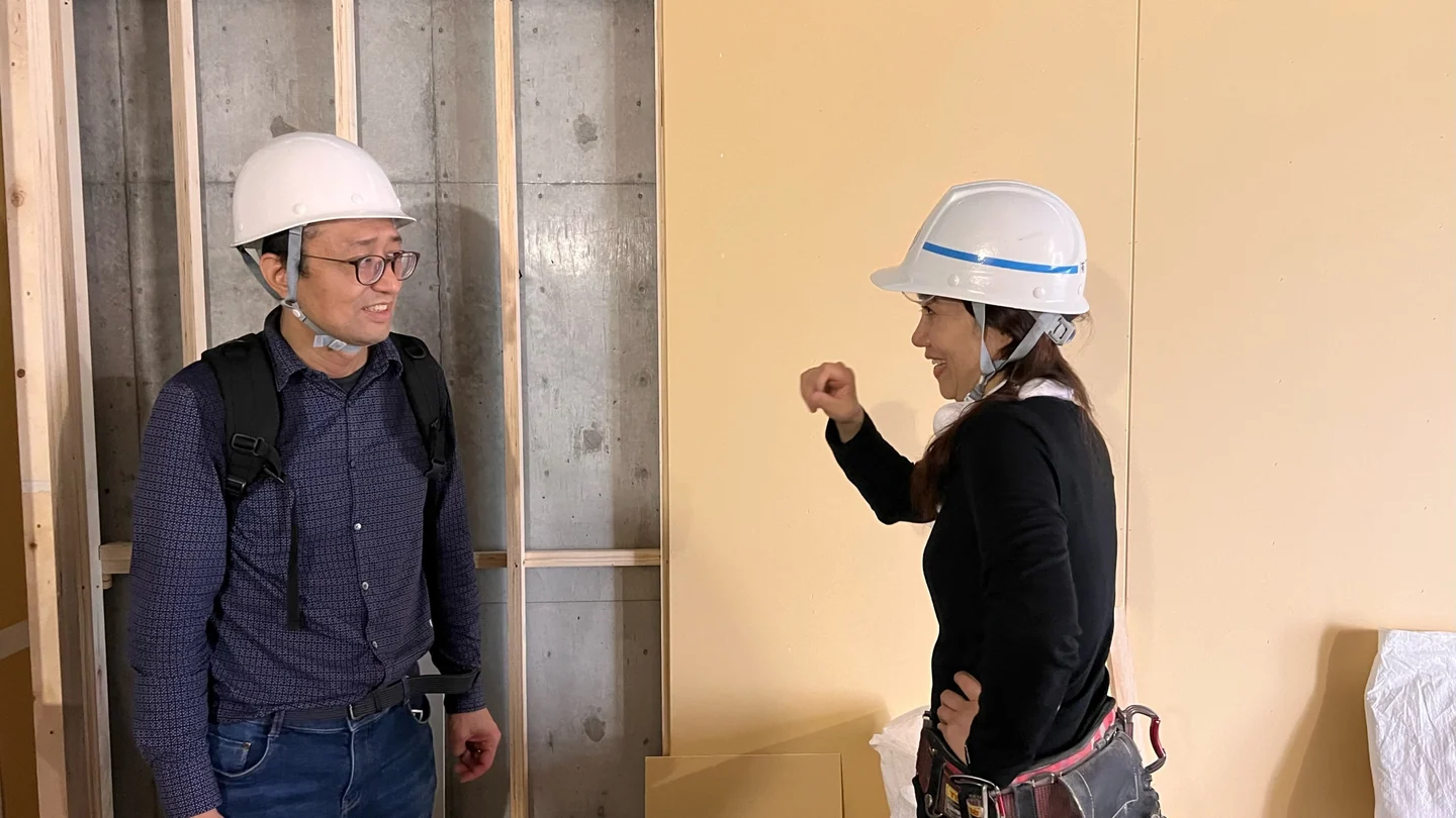 两名佩戴安全帽的人在施工现场交流,墙面构造清晰可见